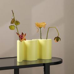 three yellow vases with flowers in them on a black table next to a gray wall