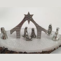 silver nativity figurines sitting on top of a piece of wood in the snow