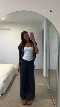 a woman taking a selfie in front of a mirror while wearing black pants and a white tank top