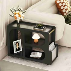 a small black shelf with pictures and flowers on it in front of a white couch