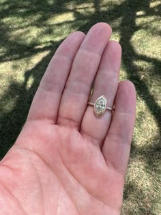 a person's hand holding a gold ring with a diamond on it in the grass