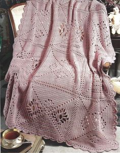 a pink crocheted blanket sitting on top of a chair next to a table