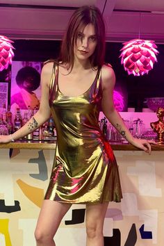 a woman standing in front of a bar wearing a gold dress