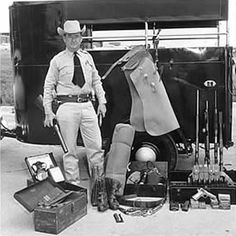 a black and white photo of a man standing in front of a truck with items on it