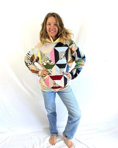 a woman standing in front of a white backdrop wearing jeans and a sweater with an abstract design on it