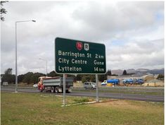 there is a large green sign on the side of the road that says barrrington st 2 km city centre gone