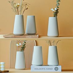 three white vases with flowers in them sitting on a shelf next to each other