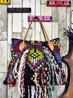 a multicolored handbag hanging from a hook on a wooden wall next to a plant