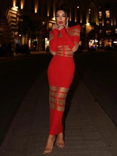 a woman in a red dress posing on the street at night with her hand on her face