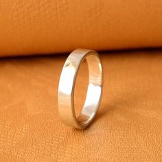 a silver ring sitting on top of a brown leather surface next to an orange pillow