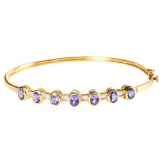 Indulge in the epitome of luxury with this exquisite 14K Yellow Gold Alternating Bezel Set Tanzanite and Diamond Bangle Bracelet. The stunning oval-shaped tanzanite gemstones are beautifully complemented by 24 natural baguette diamonds, totaling 1/5 cttw. The H-I color and VS2-SI1 clarity of the diamonds are sure to catch the eye of anyone in your presence. The alternating bezel setting of the tanzanite and diamonds lends an air of sophistication to this already elegant piece. The bracelet fits Yellow Gold Oval Bracelet With Multi-stone, Luxury Purple Oval Bracelets, Luxury Tanzanite Bracelets Gift, Luxury Tanzanite Jubilee Bracelet, Oval Tanzanite Gemstones In Yellow Gold, Diamond Bangle Bracelet, The Bangles, Diamond Bangles Bracelet, Tanzanite Gemstone