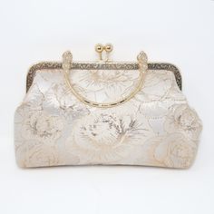 a white purse with gold trim and flowers on the front, sitting on a white surface