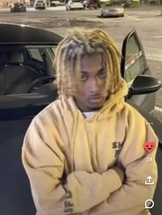 a man with dreadlocks standing in front of a car