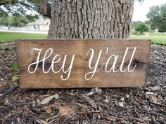 a wooden sign that says hey y'all next to a tree