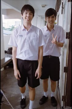 two young men standing next to each other in front of a door with their hands up