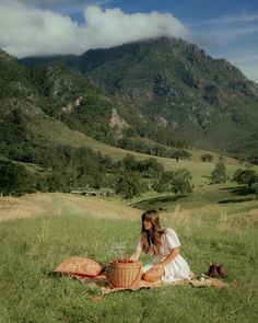 a woman sitting on top of a grass covered field next to a basket filled with food