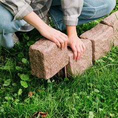 a person kneeling down on the grass with their hand on a brick block in front of them