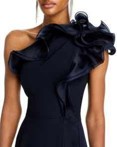 a woman wearing a black dress with ruffles on the shoulders and one shoulder