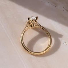 a yellow gold engagement ring with three diamonds on the top and bottom, sitting on a white surface