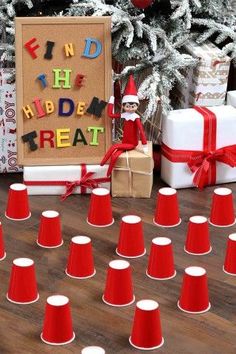 an elf sitting in front of a christmas tree surrounded by small red and white cones