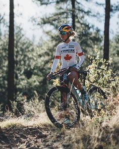 a man riding on the back of a bike down a dirt road next to trees