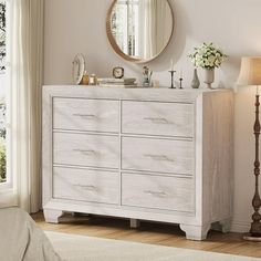 a white dresser sitting in a bedroom next to a lamp and a mirror on the wall