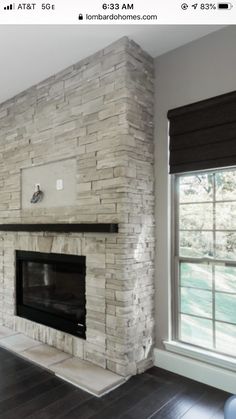 a living room with a large stone fireplace and hardwood floors in front of two windows