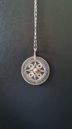 Crafted from fine silver wires reminiscent of lace and carefully crafted by hand into an elegant design with delicate swirls that meet in the middle to form a dainty flower. It comes with a sterling silver 57 cm (22.5'') chain. The necklace weighs 6g, pendant has a diameter of 3.3cm there is a glue-like small smudge, but other than that in excellent condition. Filigree, the delicate and intricate metalwork of fine wires and beads, is a hallmark of Bulgarian silver craftsmanship. Filigree is ofte Elegant Metal Necklaces With Flower Shape, Elegant Filigree Medallion Jewelry, Elegant Filigree Round Pendant Jewelry, Elegant Round Wire Wrapped Jewelry, Elegant Necklaces With Intricate Flower Pendant, Elegant Medallion Necklace With Intricate Design, Elegant Necklaces With Flower Pendant And Intricate Design, Elegant Silver Spiral Jewelry, White Gold Filigree Round Necklace