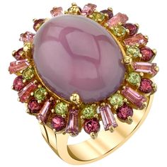 A large, 13.56 carat lavender chalcedony cabochon is featured in this one-of-a-kind cocktail ring. Fine quality, high domed and richly colored lavender chalcedony is rare, especially in large sizes. Pink tourmaline tapered baguettes, mulberry rhodolite garnets and apple green peridots encircle the chalcedony. This selection of pastel gemstones create a colorful frame for the chalcedony reminiscent of an Impressionistic masterpiece. Made of 18k yellow gold by our artisans in Los Angeles. This fun Lavender Cocktail, Month Gemstones, Yellow Gold Cocktail Ring, Colorful Frames, Gold Cocktail Ring, Gold Cocktail, Gemstone Engagement, Green Gems, Rhodolite Garnet