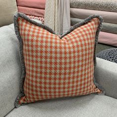 an orange and white pillow sitting on top of a gray couch next to a pile of pillows