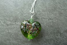 A sterling silver chain which features a handmade lampwork glass pendant. The pendant bead is a green and brown speckled heart and is strung with swarovski crystals. Green Sterling Silver Heart Jewelry, Green Heart-shaped Sterling Silver Jewelry, Sterling Silver Jewelry With Heart Charm In Green, Green Sterling Silver Heart Pendant Necklace, Green Heart-shaped Sterling Silver Necklace, Green Sterling Silver Necklace With Heart Charm, Nickel-free Green Heart Necklace, Green Heart-shaped Nickel-free Necklace, Handmade Green Heart Pendant Jewelry