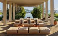 an outdoor living area with couches and tables on the ground next to some water