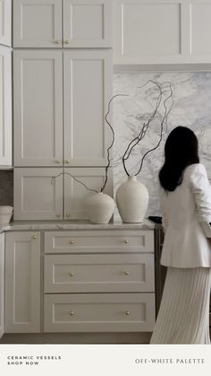 a woman is standing in the kitchen looking at something on the counter top and cupboards