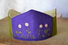 a close up of a purple and green paper crown with flowers on the front, sitting on a wooden surface