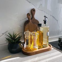 a cutting board with two bottles of olive oil on it next to a potted succulent