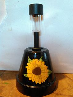 a black vase with a yellow sunflower painted on it's side sitting on a wooden table