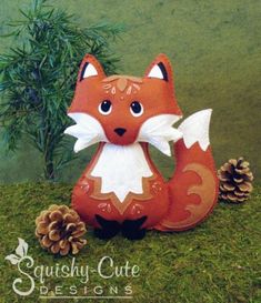 a stuffed fox sitting next to a pine cone on top of a green grass covered field