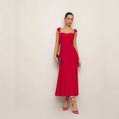 a woman in a red dress stands against a white wall