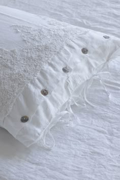 a white pillow with buttons on it sitting on top of a bed covered in white sheets