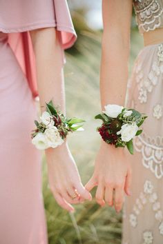 two women in pink dresses holding hands with flowers on their wrist and wearing matching bracelets