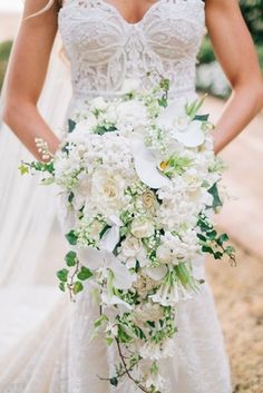 the bride is holding her bouquet with white flowers and greenery on it's side