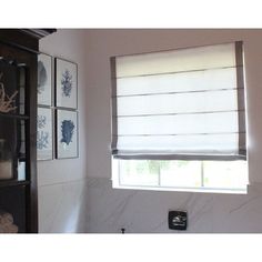 a bathroom with white walls and marble counter tops, including a window that has roman shades on it