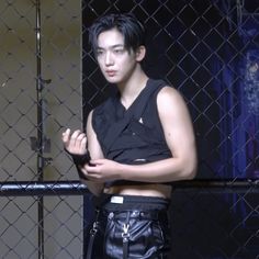 a man standing in front of a chain link fence with his arms crossed and looking off to the side