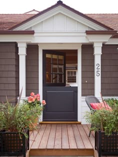 the front door is open and there are flowers in pots on the porch next to it