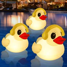 three yellow rubber ducks floating on top of a blue swimming pool with lights around them