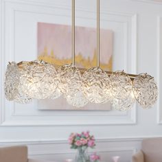 a chandelier hanging over a dining table in a room with white walls and beige chairs