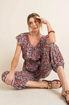 A comfortable jumpsuit with a pop of red and sprinkle of flowers. This jogger style jumpsuit has an elastic waistline, shaping the loose, lightweight fabric. There is a ruffled fabric detail along the neckline and sleeves, and side pockets. Style with sandals for a picnic in the park. Model is 5'10" and wearing her true size Small. Small: Bust 18", Length 54.5" 100% Rayon Casual Red Overall Jumpsuits And Rompers, Summer Floral Print Relaxed Fit Jumpsuits And Rompers, Casual Printed Jumpsuits And Rompers For Spring, Red Relaxed Fit Jumpsuits And Rompers For Summer, Red Relaxed Fit Jumpsuit For Summer, Casual Printed Relaxed Fit Jumpsuits And Rompers, Printed Casual Relaxed Fit Jumpsuits And Rompers, Casual Relaxed Fit Printed Jumpsuits And Rompers, Casual Floral Print V-neck Jumpsuits And Rompers