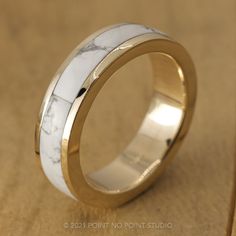 a white marble ring with gold inlays on it's side, sitting on a wooden surface