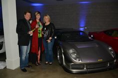 three people standing next to a sports car