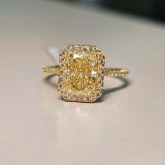 a fancy yellow diamond ring sitting on top of a white surface with diamonds around it